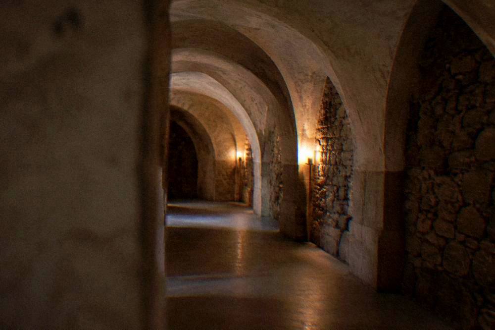 A candle-lit underground corridor of stacked bones in the Brno Ossuary