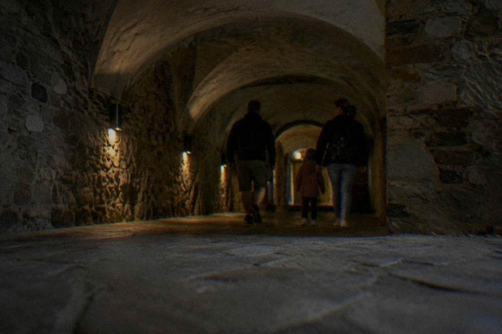 Family entering a dimly lit stone underground corridor with arched ceilings