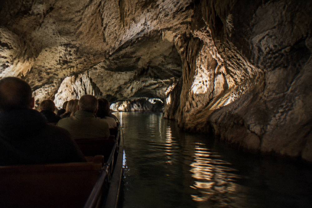 Boat carrying visitors along an underground river inside a lit limestone cave
