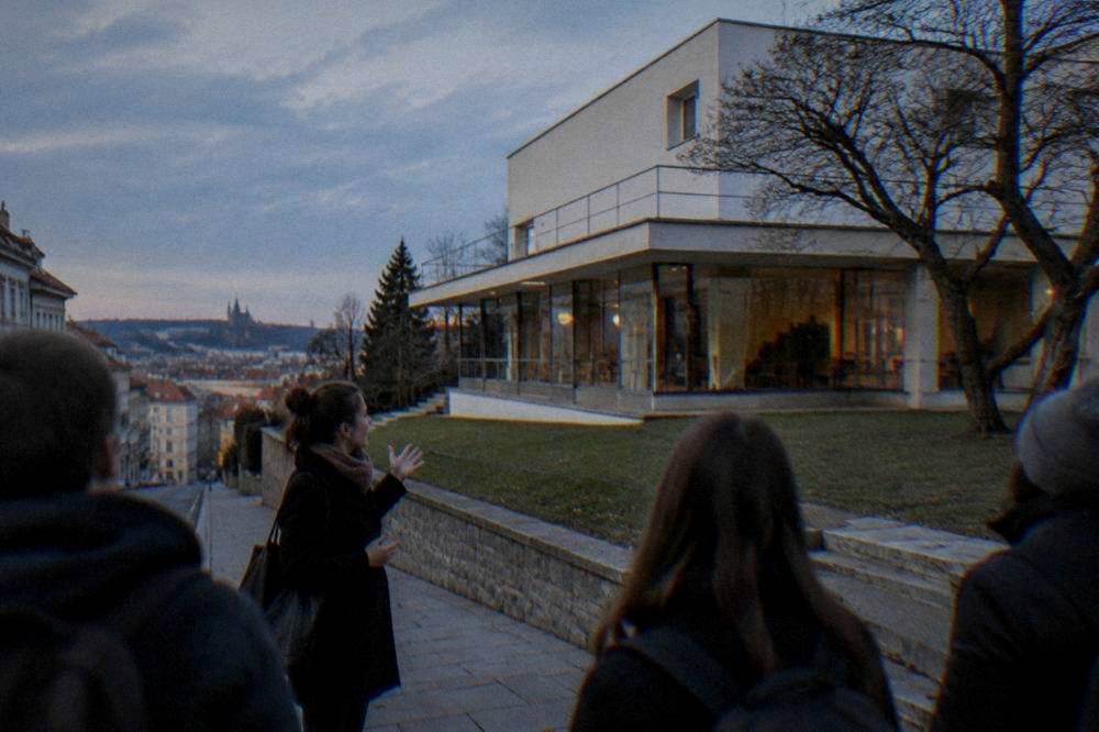 A tour guide speaking to a small group on a city street in front of a modernist building