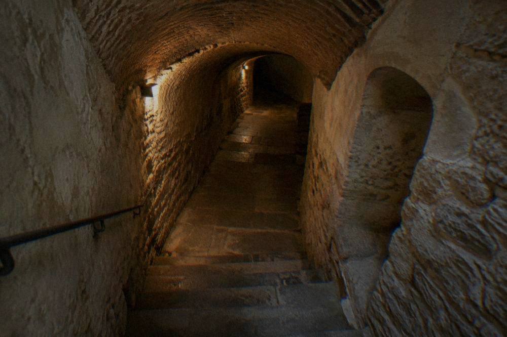 Stacked and arranged human bones displayed on shelves in a dimly lit underground ossuary chamber