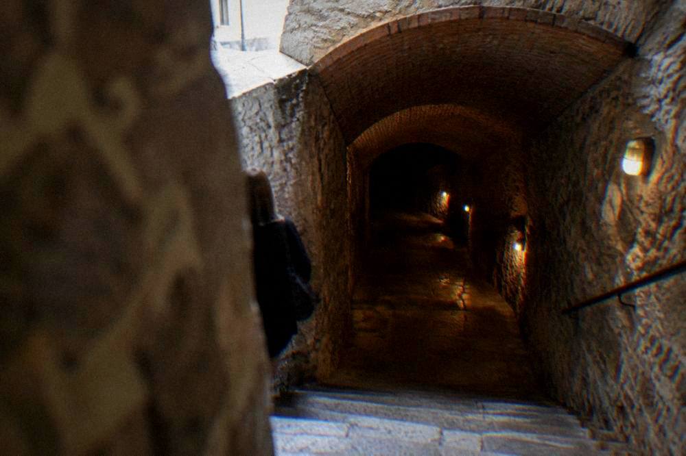 Stone stairway descending from a sunlit street into a brick vaulted underground passage
