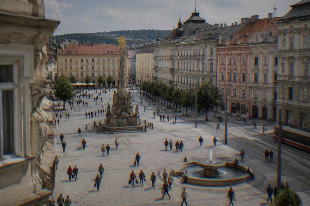 Crowd of pedestrians crossing Freedom Square in Brno with the plague column and pastel facades