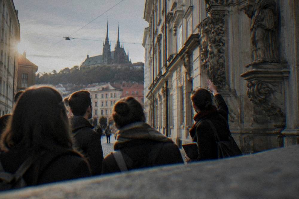Guide pointing out carvings on a historic building facade to a group in Brno