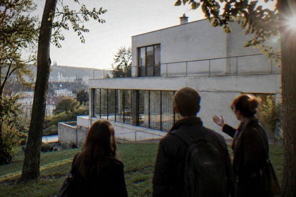 A private guide showing two visitors the facade of a functionalist villa in Brno
